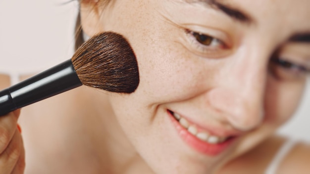 Una giovane bella ragazza bianca con una spazzola per il trucco si mette il trucco sul viso. Cipria per il viso.