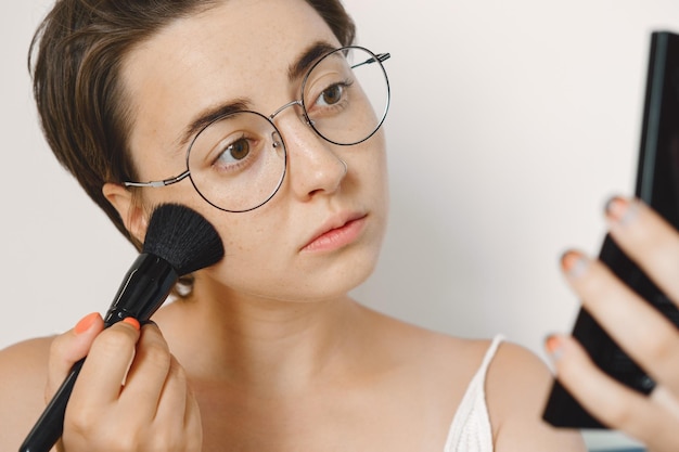 Una giovane bella ragazza bianca con una spazzola per il trucco si mette il trucco sul viso. Cipria per il viso.