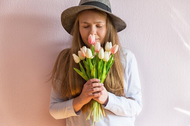 Una giovane bella ragazza con i capelli lunghi biondi sciolti e un cappello di feltro in testa tiene i fiori di primavera