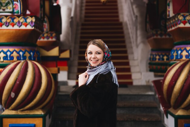 Una giovane bella ragazza con un cappotto di visone e una sciarpa popolare russa passeggia intorno al Cremlino di Izmailovo. Mosca, Russia.