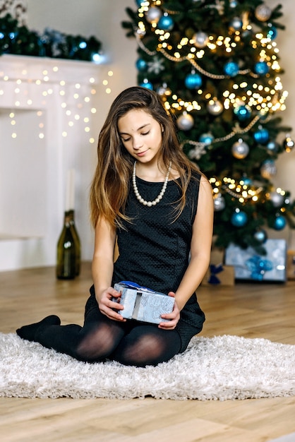 Una giovane bella ragazza con un regalo tra le mani vicino all'albero di Capodanno sorride con gioia