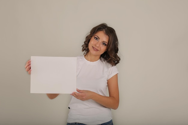 una giovane bella ragazza dai capelli castani con una maglietta bianca tiene in mano un foglio di carta bianco