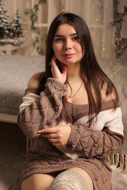 una giovane bella ragazza dai capelli castani è seduta vicino al letto con un maglione lavorato a maglia
