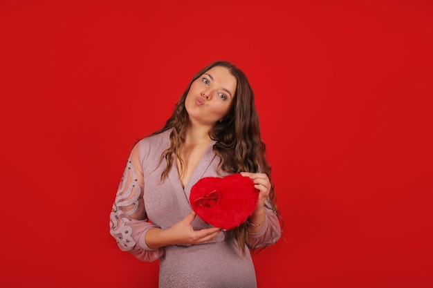 una giovane bella ragazza in un abito rosa sullo sfondo tiene in mano una confezione regalo per le vacanze