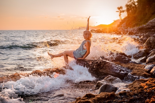 Una giovane bella ragazza spruzza e spruzza il mare al tramonto.