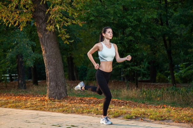 Una giovane bella ragazza sta correndo nel parco durante la stagione fredda al parco. .