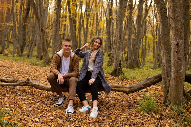 una giovane bella ragazza sta dietro a un ragazzo seduto su un albero caduto nella foresta autunnale della città