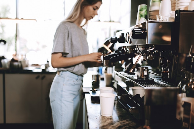 Una giovane bionda piuttosto magra, vestita in modo casual, sta cucinando il caffè in una famosa caffetteria. .