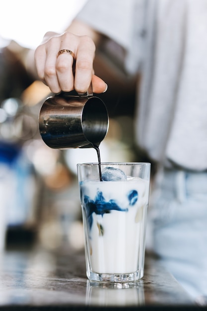 Una giovane bionda piuttosto snella, che indossa un abbigliamento casual, versa il caffè in un bicchiere di latte in un'accogliente caffetteria. .