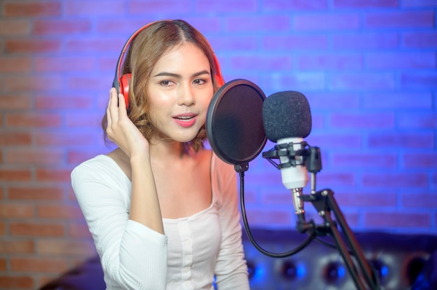 Una giovane cantante sorridente che indossa le cuffie con un microfono mentre registra una canzone in uno studio musicale con luci colorate.