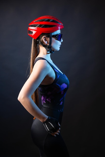 Una giovane ciclista femminile che indossa un casco di sicurezza e occhiali vestiti con pantaloncini si pone su uno sfondo nero in studio