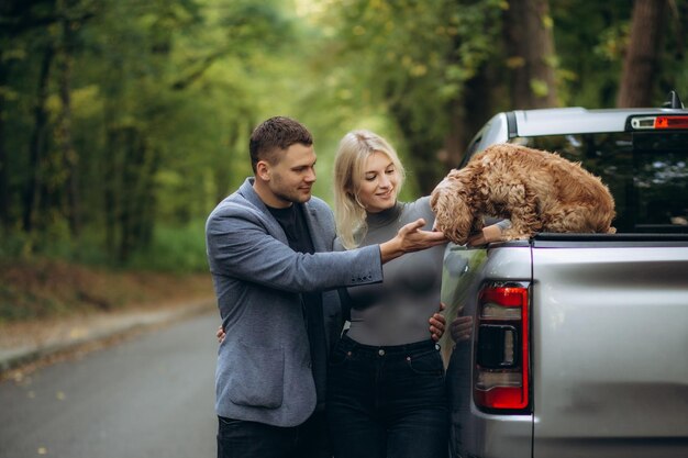 una giovane coppia accarezza un cane seduto su un'auto