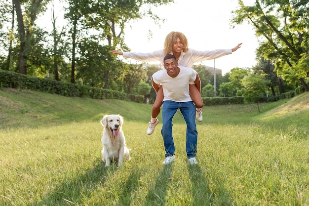 Una giovane coppia afroamericana innamorata corre con il cane nel parco e sorride