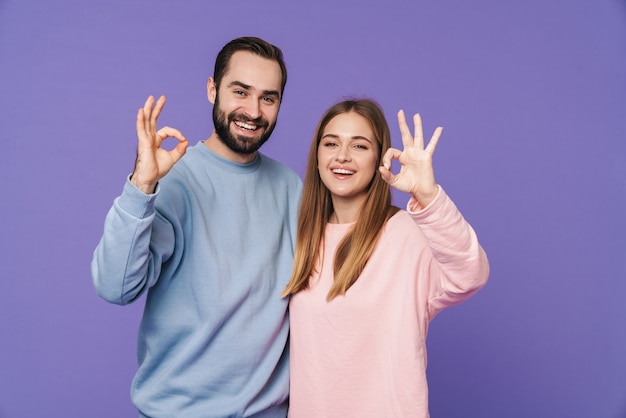 una giovane coppia amorosa sorridente positiva isolata sopra la parete viola che mostra il gesto giusto.