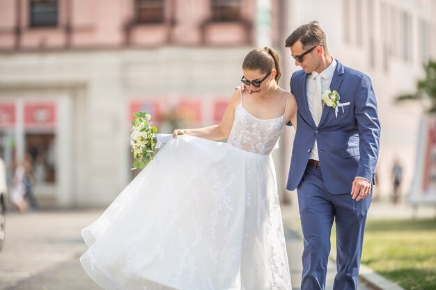 Una giovane coppia appena sposata che cammina felicemente in città in abiti da sposa con un bellissimo bouquet.