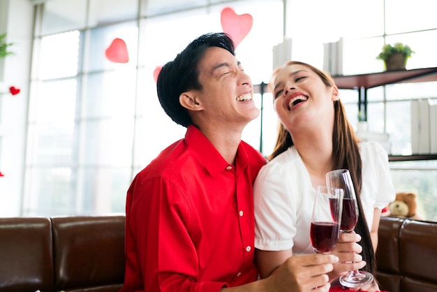 Una giovane coppia asiatica felice che parla e ride mentre beve vino rosso insieme nel suo anniversario