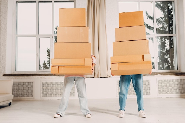 Una giovane coppia di coppia felice, un uomo e una donna, si trasferiscono con una pila di scatole di cartone in un nuovo appartamento.