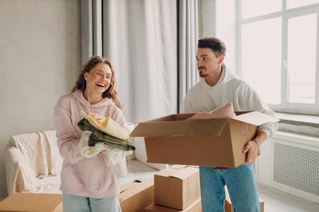 Una giovane coppia di famiglie felici, un uomo e una donna, spacciano la scatola dopo aver spostato le scatole di cartone nel nuovo appartamento.