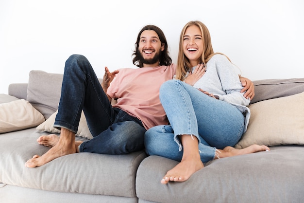 una giovane coppia di innamorati felice sul divano guarda film tv al chiuso a casa.