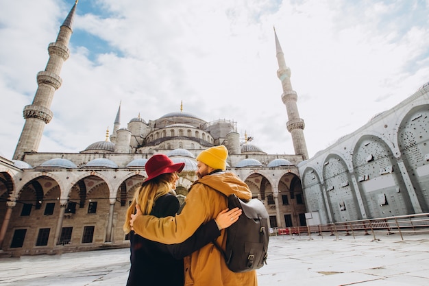 Una giovane coppia europea cammina nel cortile della Moschea Blu di Istanbul, in Turchia. Il tipo e la ragazza del viaggiatore in cappelli gialli camminano nell'inverno Istanbul. nuvoloso giorno d'autunno a Istanbul.