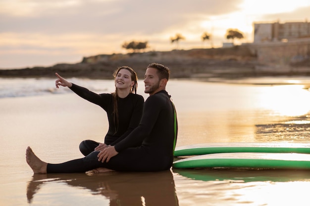 Una giovane coppia felice che si rilassa sulla spiaggia dopo una giornata di surf