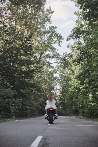 Una giovane coppia felice guida una moto su una strada asfaltata nella foresta libertà e velocità sul retro
