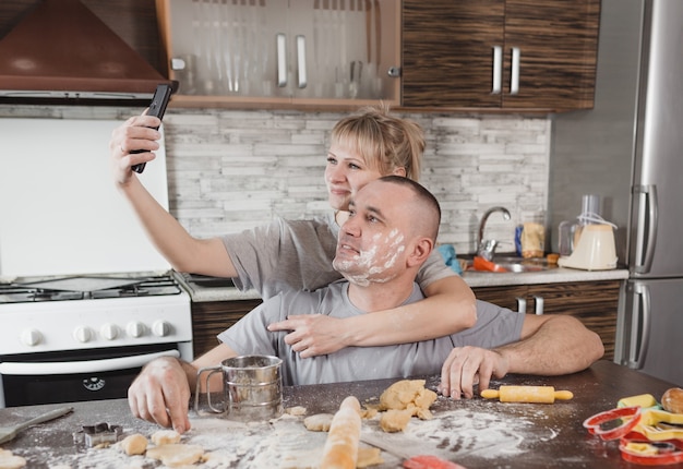 Una giovane coppia felice imbrattata di farina si fa un selfie in cucina. marito e moglie felici e amorevoli