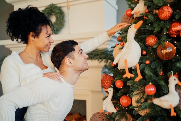 Una giovane coppia felice si sta preparando per il Natale Decorare l'albero di Natale con i giocattoli Le vacanze di Capodanno alla vigilia