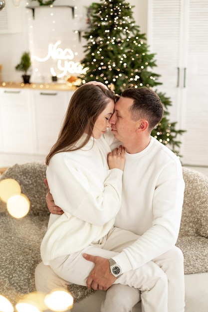 una giovane coppia felice un ragazzo e una ragazza si baciano e si abbracciano congratulandosi a vicenda per il nuovo anno sullo sfondo di un albero di Natale