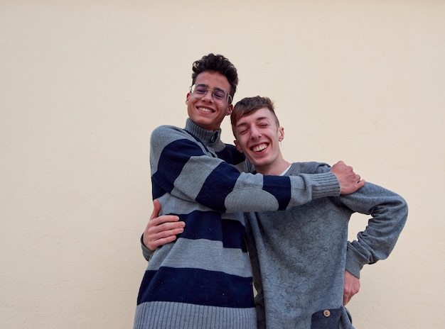 Una giovane coppia gay interrazziale che si abbraccia felicemente isolata su uno sfondo beige
