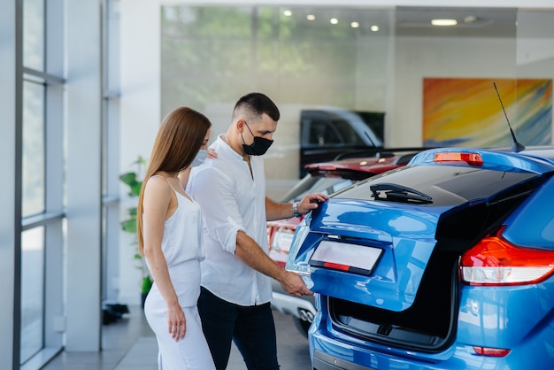 Una giovane coppia in maschera seleziona un nuovo veicolo e consulta un rappresentante della concessionaria nel periodo della pandemia. Vendite di automobili e vita durante la pandemia.