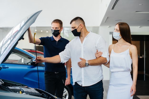 Una giovane coppia in maschera seleziona un nuovo veicolo e consulta un rappresentante della concessionaria nel periodo della pandemia. Vendite di automobili e vita durante la pandemia.