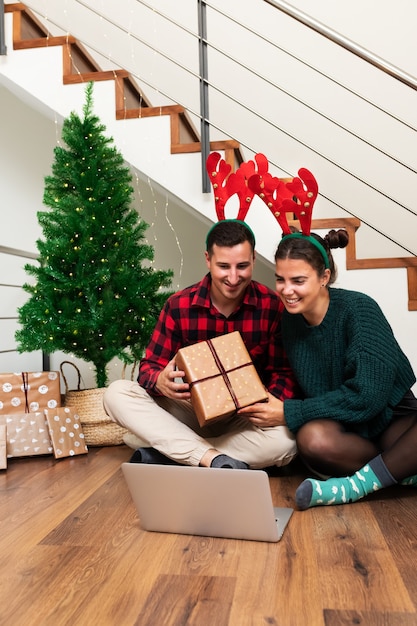 Una giovane coppia indossa corna di renna durante una videochiamata che mostra il regalo di Natale alla famiglia Vertical