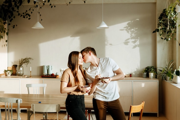 Una giovane coppia innamorata fa colazione insieme a casa in cucina. Uomo e donna che mangiano cereale con latte per la prima colazione.