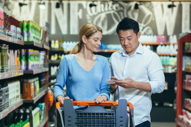 Una giovane coppia internazionale, una donna e un uomo asiatico sono in piedi in un supermercato nel