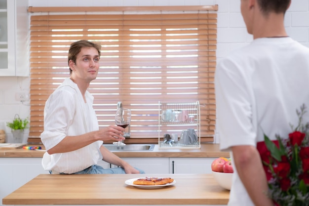 Una giovane coppia LGBT celebra il giorno dell'amore con un bicchiere di vino nella cucina di casa loro