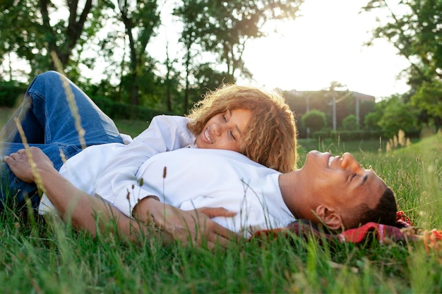 Una giovane coppia romantica afroamericana giace sull'erba del parco e dorme in natura.