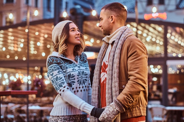 Una giovane coppia romantica che si tiene per mano e si guarda mentre si trova in strada nel periodo natalizio