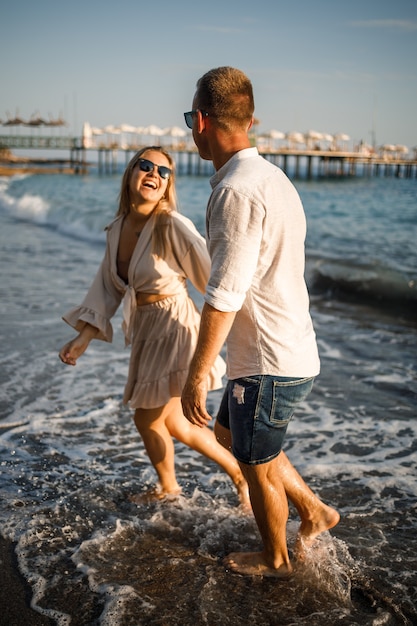 Una giovane coppia romantica innamorata insieme sulla sabbia cammina lungo la spiaggia del Mar Mediterraneo. Vacanze estive in un paese caldo.