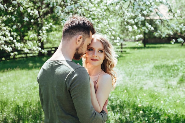 Una giovane coppia si abbraccia, la ragazza distoglie lo sguardo di lato. il concetto di una storia d'amore intorno all'erba verde e agli alberi in fiore. avvicinamento