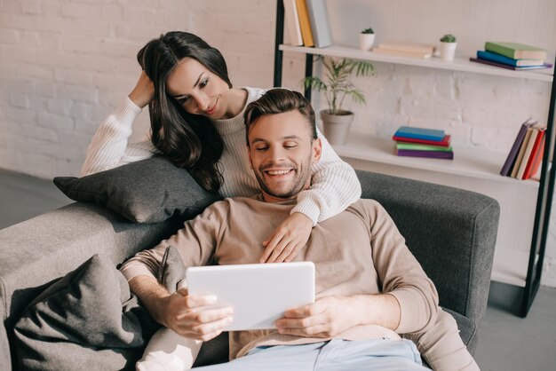 una giovane coppia sorridente che usa la tablet insieme sul divano a casa