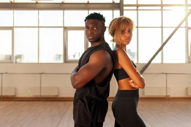 Una giovane coppia sportiva afroamericana in abbigliamento sportivo si trova con le braccia incrociate in palestra.