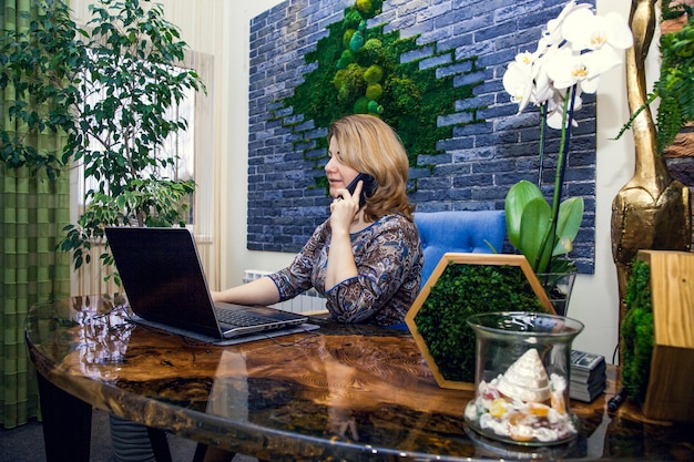 Una giovane designer d'interni sta lavorando e sta parlando al telefono nel suo ufficio davanti a un computer.