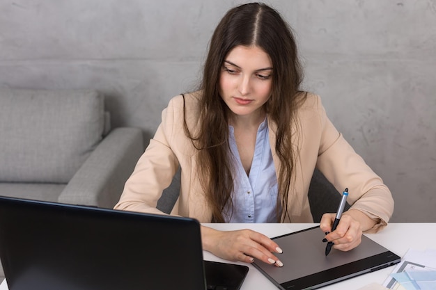 Una giovane designer ragazza seduta a un tavolo disegna su un tablet. Esegue calcoli aziendali sul computer.