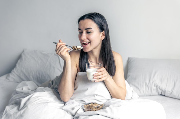 Una giovane donna a letto bianco con cereali e latte