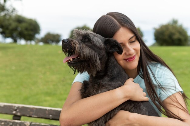 Una giovane donna adulta latina abbraccia il suo schnauzer maschio nel parco