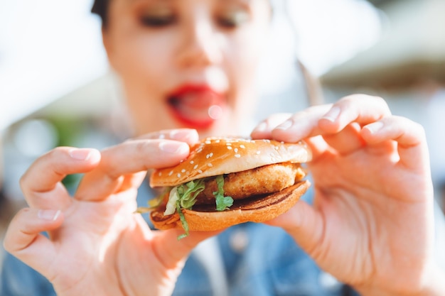 Una giovane donna affascinante con i dreadlocks e il rossetto rosso è seduta e mangia un hamburger in un caffè di strada il concetto di mangiare un rossetto a lunga durata