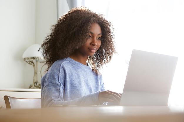 Una giovane donna africana attraente seduta a casa e che lavora al portatile.
