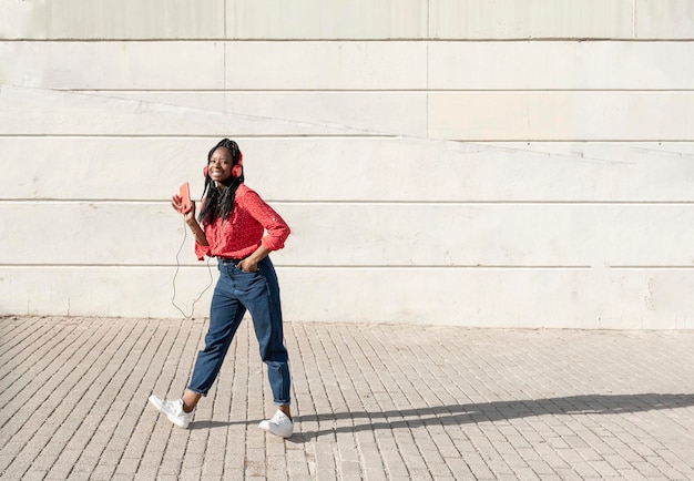 Una giovane donna afroamericana con le trecce che ascolta musica e balla per strada