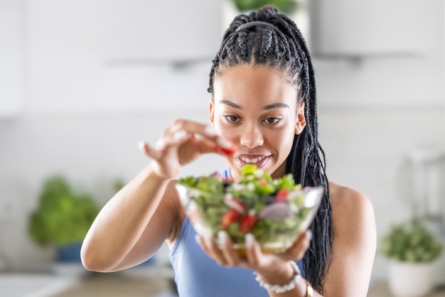 Una giovane donna afroamericana prepara un'insalata sana aggiunge i pomodori